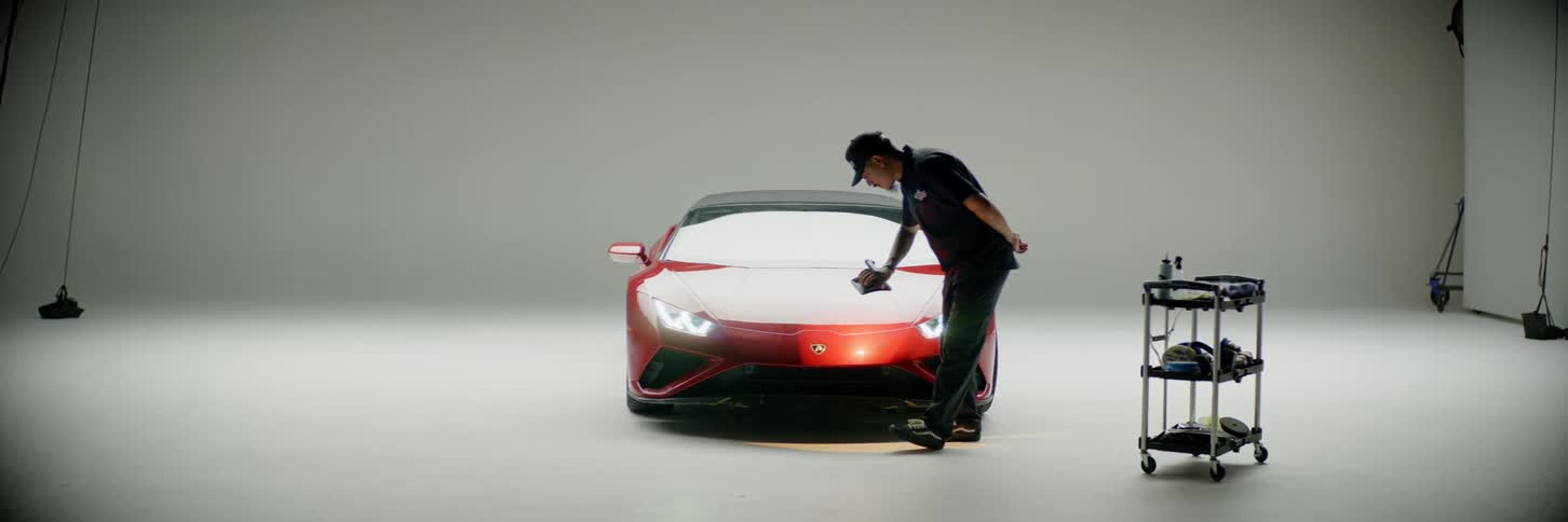 Technichian painting the hood of a sports car with spray gun inside a brightly lit all white garage