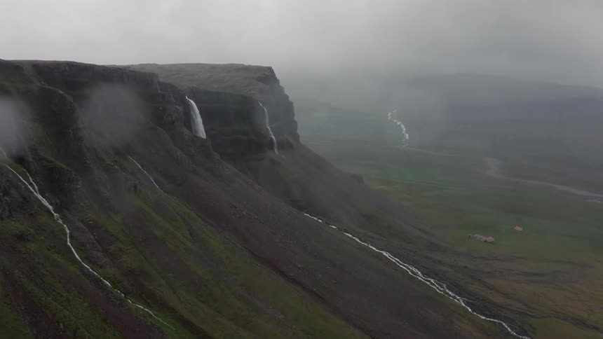 A waterfall pours over a cliff into the valley below on a foggy day