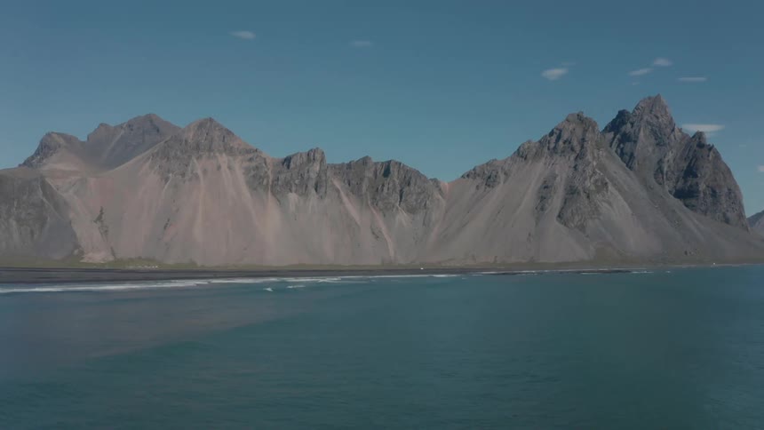 Aerial panorama of an ocean with mountains and peaks on the horizon on a day with a blue sky