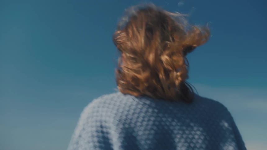 Woman walking backward in a natural setting with a blue sky
