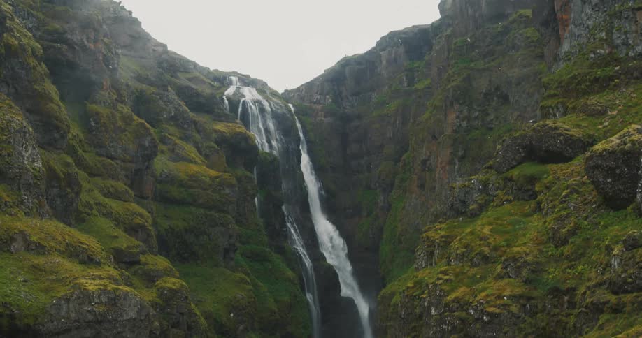 A small waterfall that starts at the top of a mountain and several birds are flying nearby