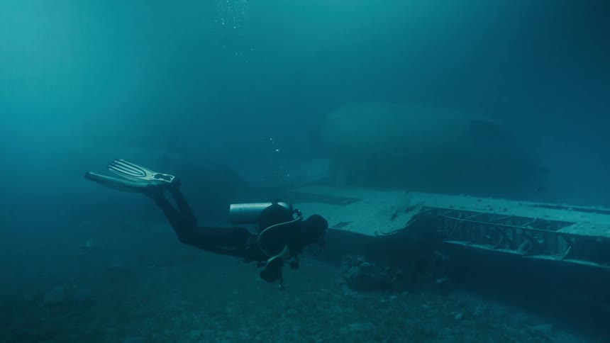 A diver at the bottom of the sea near ship wrecks
