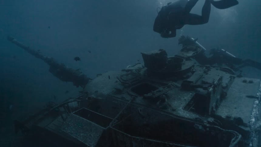 Divers at the bottom of the sea passing by a tank