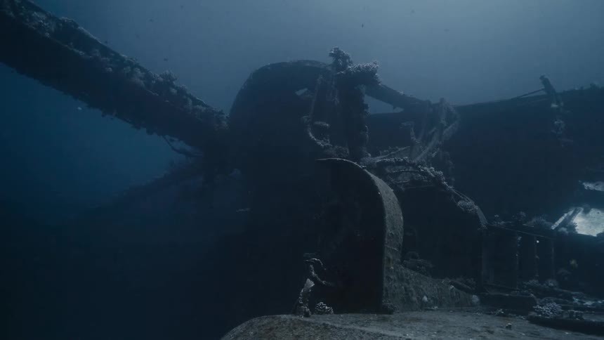 Ship wreckage of a ship with a large mast laying on its side at the bottom of ocean in murky blue water