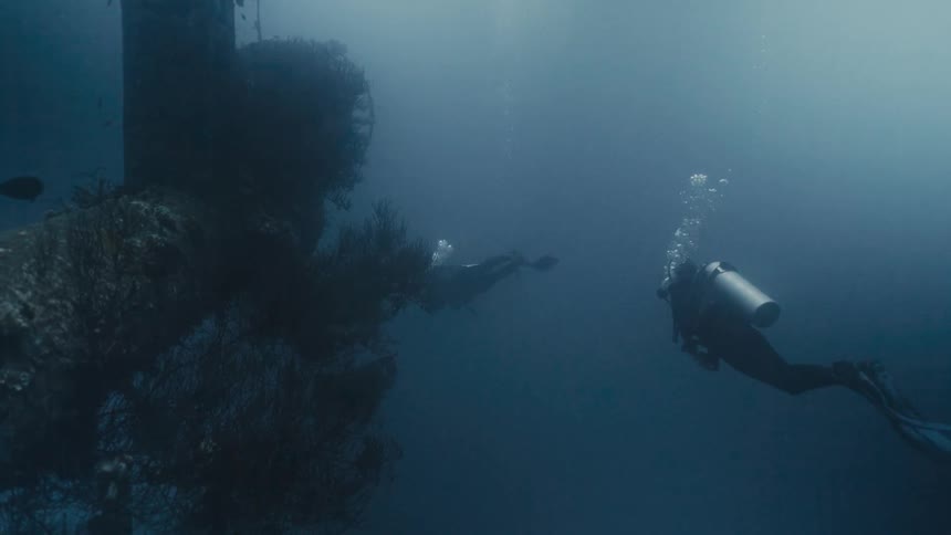 Two divers at the bottom of the sea amidst wreckage covered in sediment
