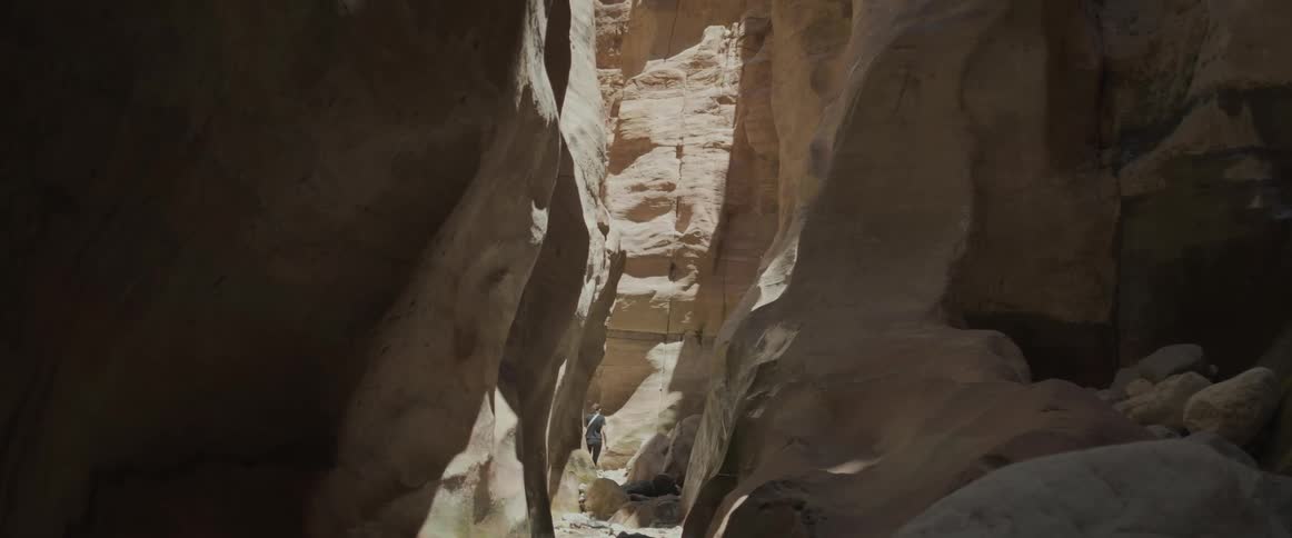 Female walks by in the sunlight of a hiking trail in a gorge between tall smooth white rocks