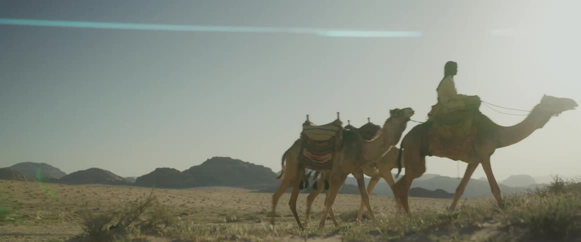 Man riding a camel in the middle of the desert with two other camels right behind