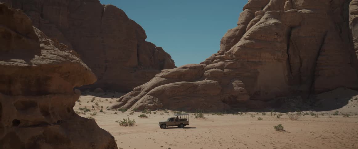 A truck driving in a desert surrounded by rock on a sunny day