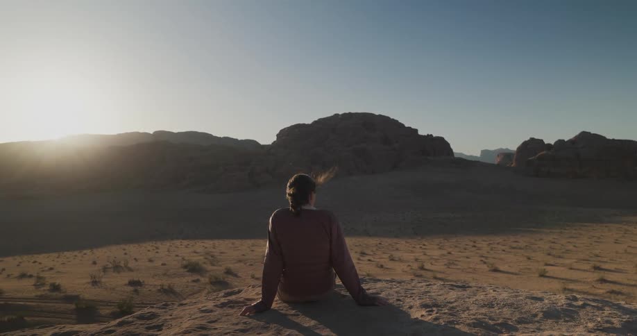 Woman sitting on a rock overlooking a desert horizon at sunset