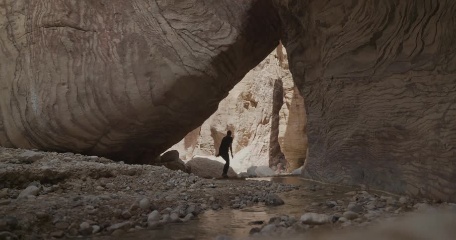A woman walking through the cave stops near a small stream