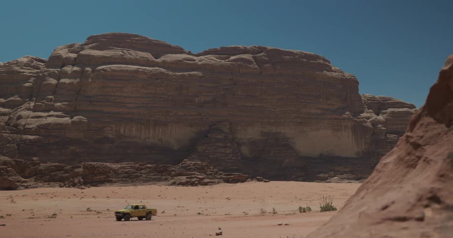 Truck driving through desert terrain next to canyons on a cloudless day with a blue sky