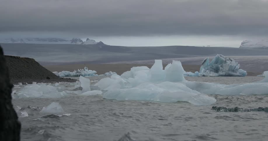 Icebergs float near a shore on a gray and cloudy day