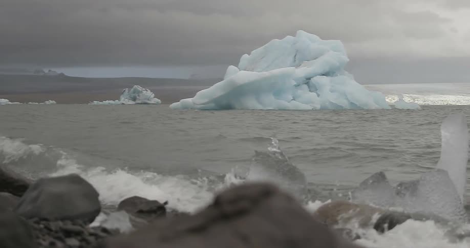 Waves crashing on a rocky beach with icebergs and dark clouds in the sky