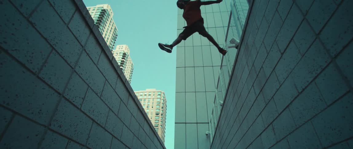 A man is jumping from the roof of one building to another