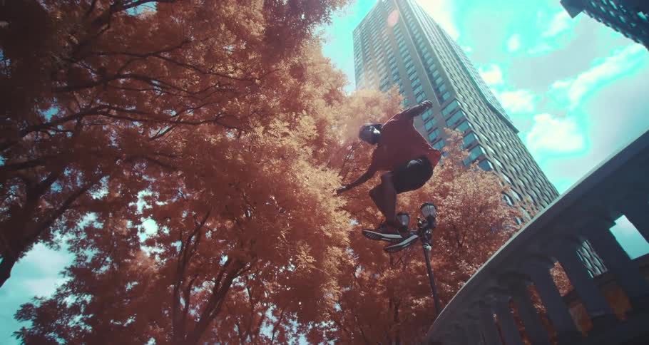 A man jumping over a concrete structure in a city with tall buildings and trees with orange leaves