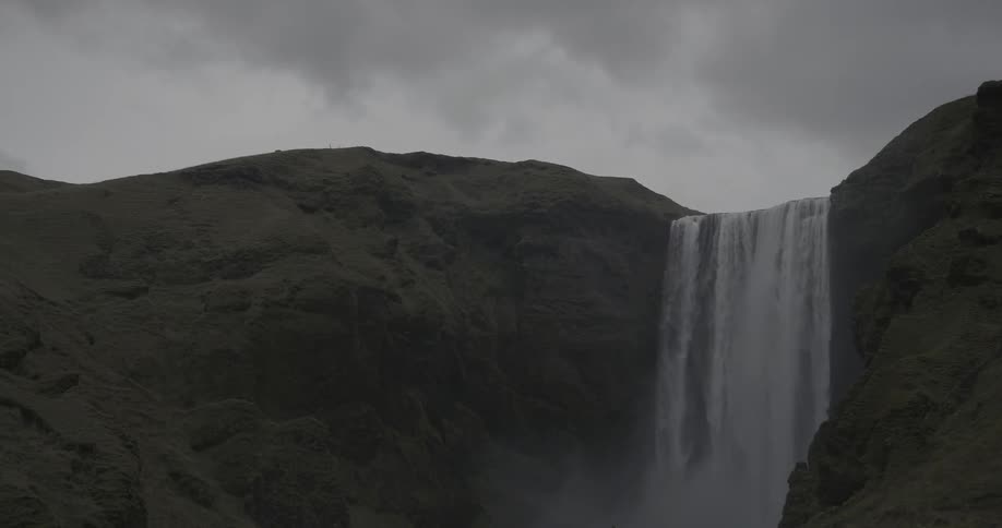 A waterfall gushes over a cliff on a cloudy day