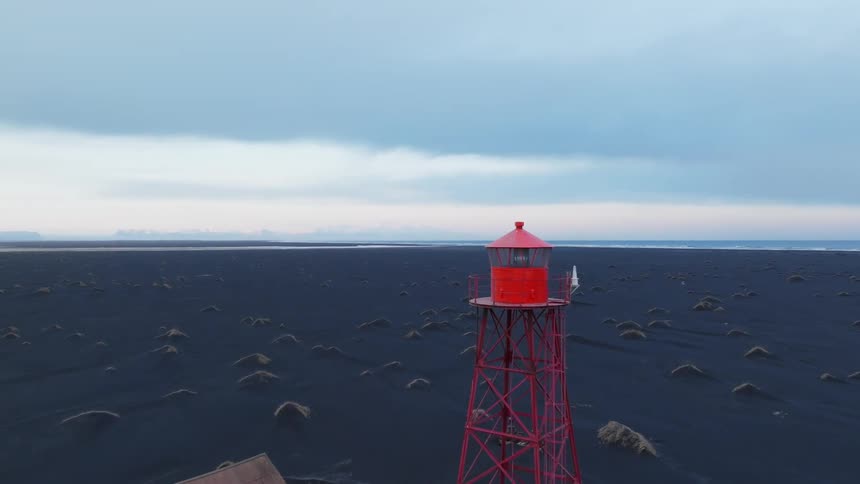 Aerial panorama of a red tower with an observation deck in the midst of a natural environment with black sand