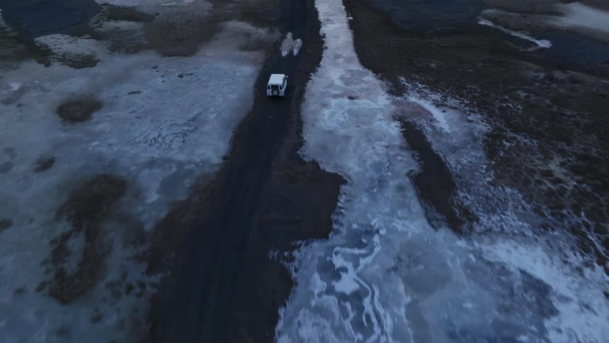 A white car on a black dirt road with large puddles of water