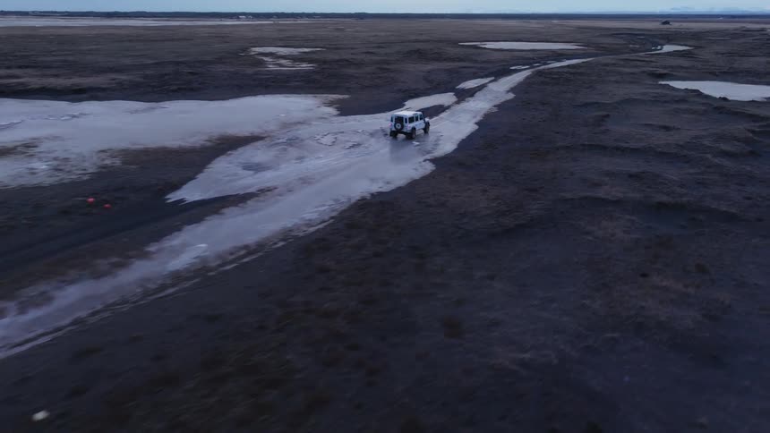 Car driving through a natural environment with black soil and frozen patches
