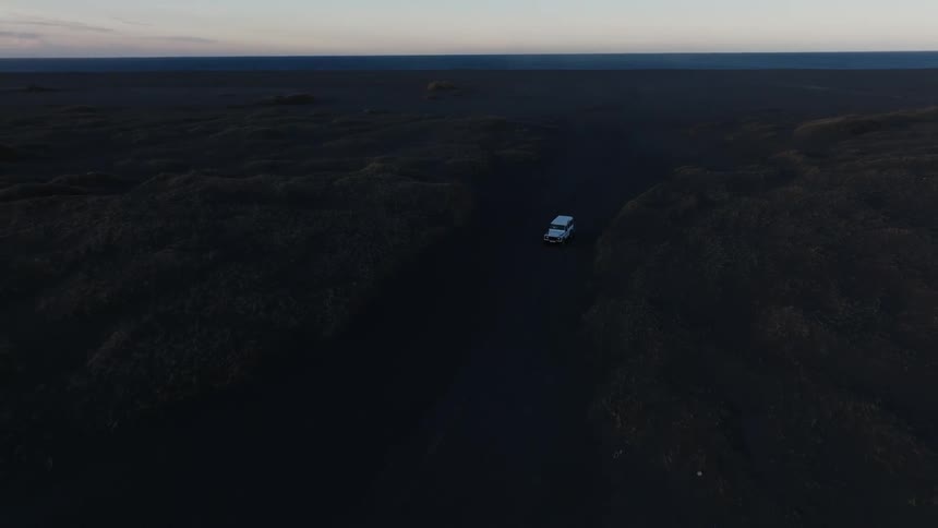 Car driving through black soil in a natural environment with a purple dawn sky