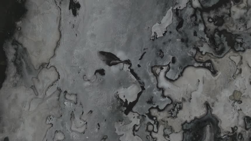 Aerial view of a frozen stillness of a lake juxtaposed against the dark expanse of a black sandy beach in iceland