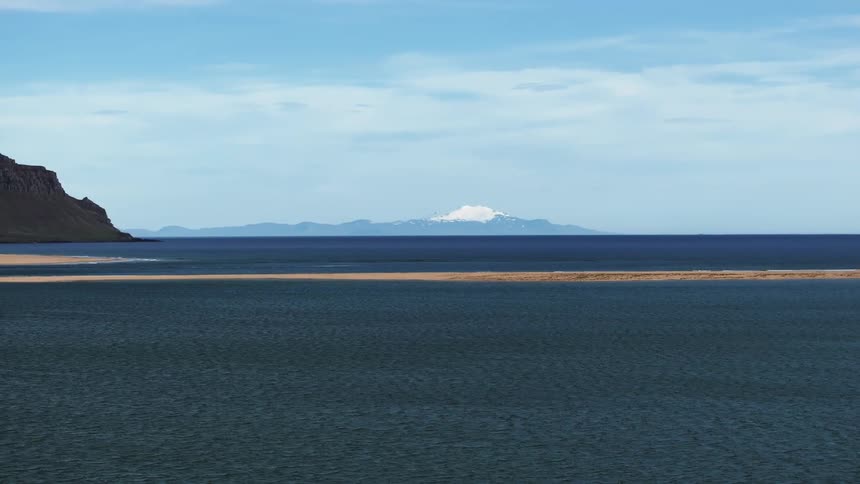 Aerial view of sandy beach near the blue ocean with a distant snowy mountain