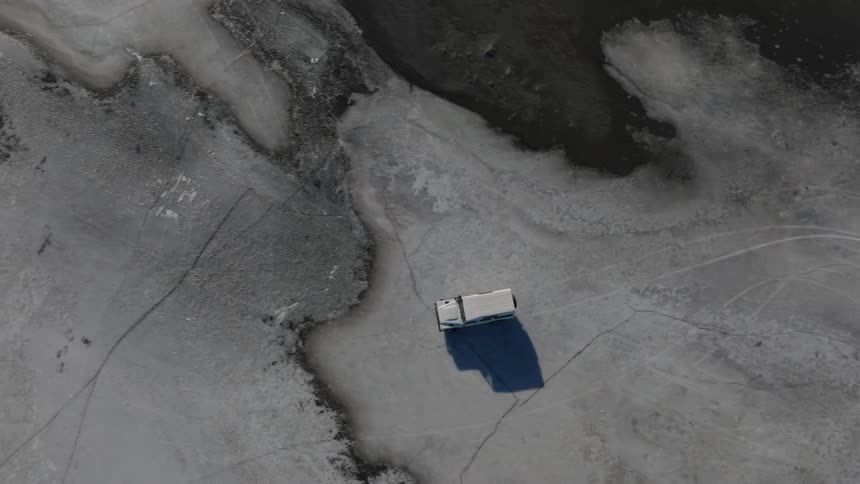 A white jeep kicks up desert sand as it drifts across the arid landscape from above