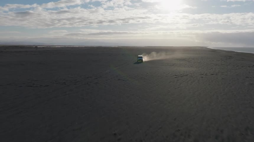 Aerial of white jeep driving on the beach at sunset
