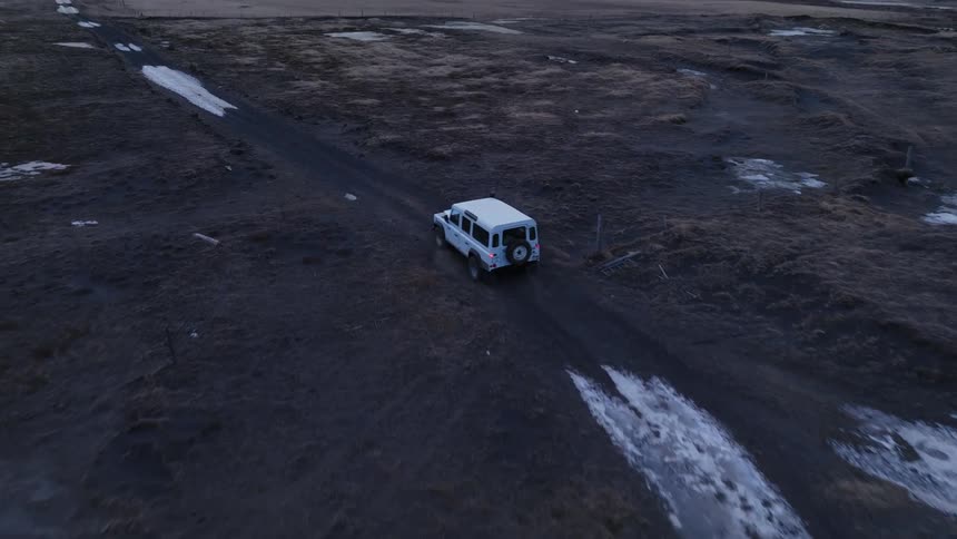 Aerial view of a white jeep driving down a dirt road in the field in iceland