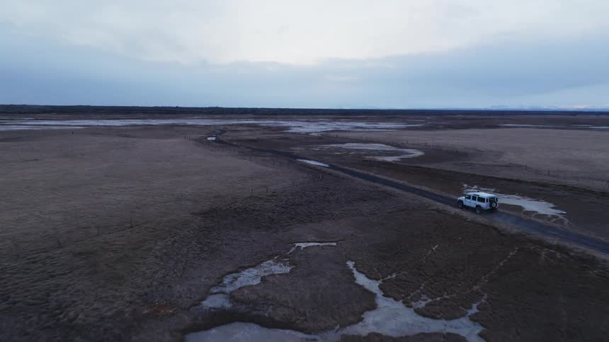 A white car on a dirt road with large puddles of water