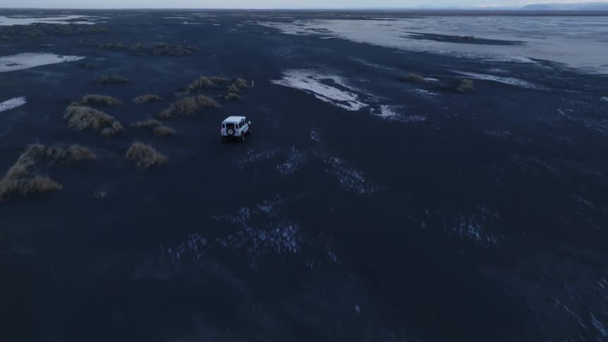 Aerial panorama of a jeep driving on black ground with frozen patches on a morning