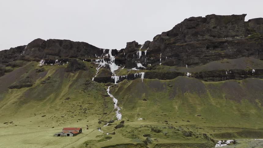 Aerial of a solitary house stands close to a rugged mountain ridge