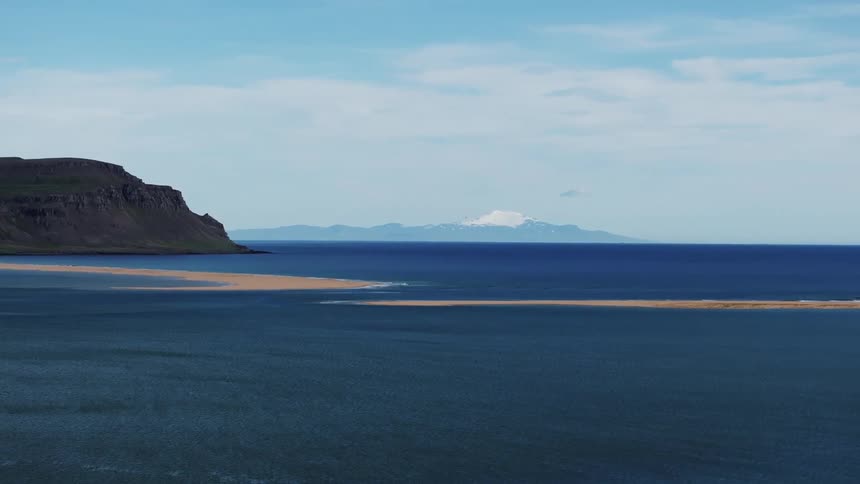 A sandy beach stretches along the waters edge with a distant mountain completing the serene scene
