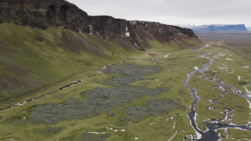 Aerial view of streams stretch across the green field near the mountain ridge