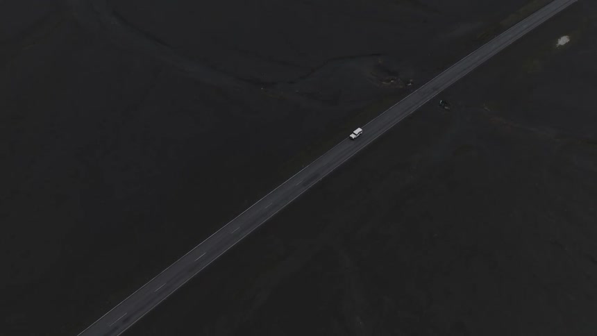 Aerial of a a white jeep cruising along a road navigating through the mesmerizing black sand field of iceland