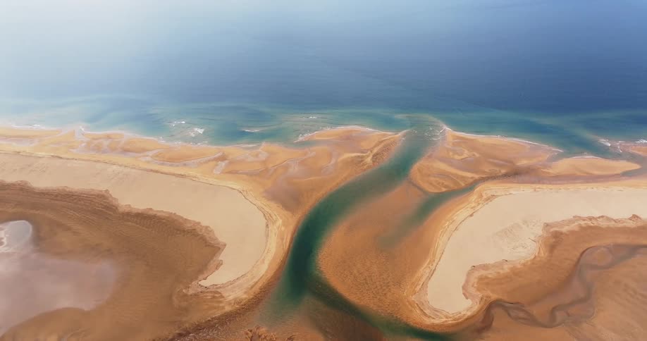 Aerial of a river gracefully winding through golden sands before merging with the crystalclear azure waters of the ocean