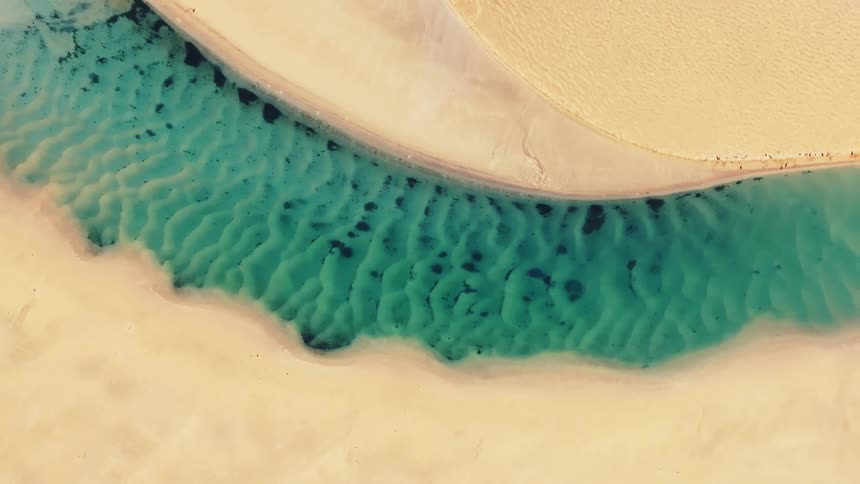 Aerial of a light blue riverbed cutting through a sandy beach