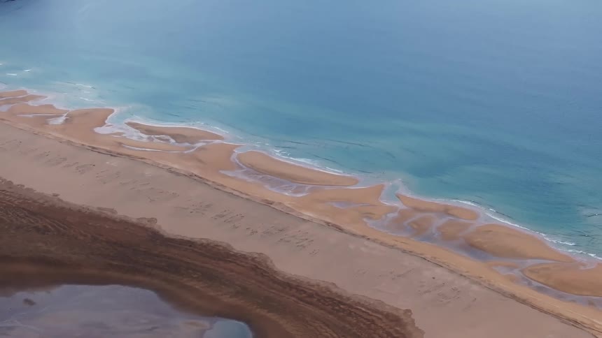 Aerial view of the golden grains of sand meeting the clear azure waters of the ocean