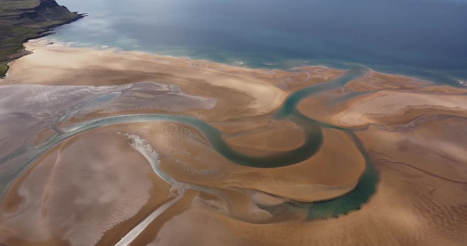 An aerial view of a river flowing through a sandy beach and into the ocean