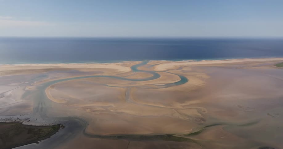 Aerial view of a river gracefully winding through golden sands before merging with the crystalclear azure waters of the ocean