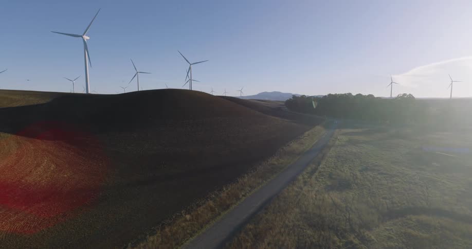 A road runs through a wind farm with turbines on the hills and a mountain in the distance