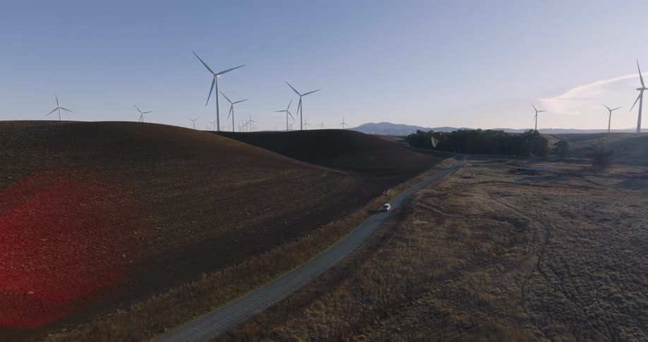 Aerial view of car driving on a country road with wind turbines in the background