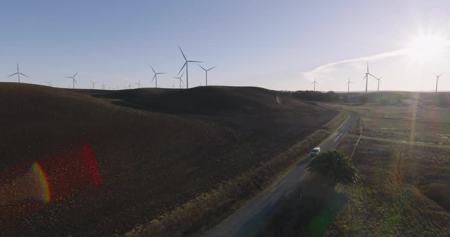 Car driving on a road beside a grassland with wind energy platforms