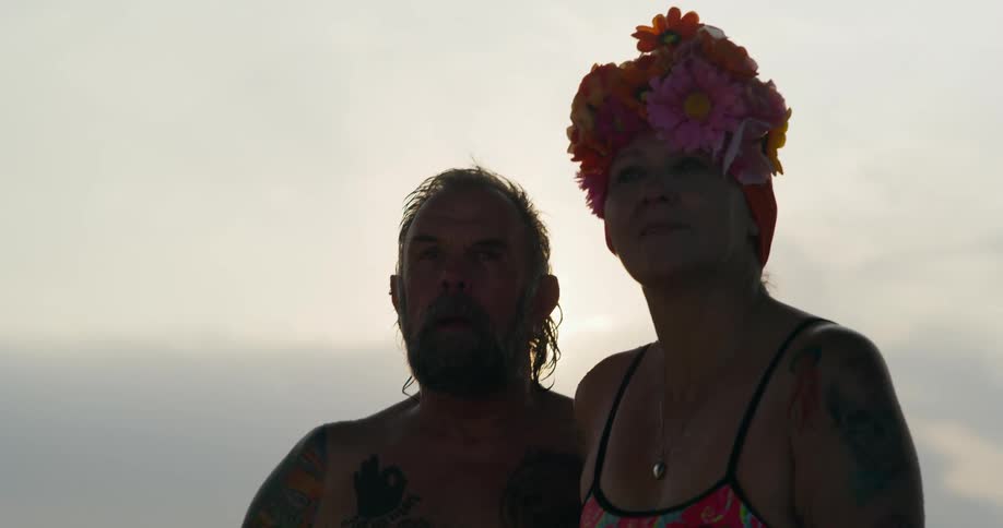 A middle aged couple in bathing suits looks at something intently then turns around and heads in the opposite direction