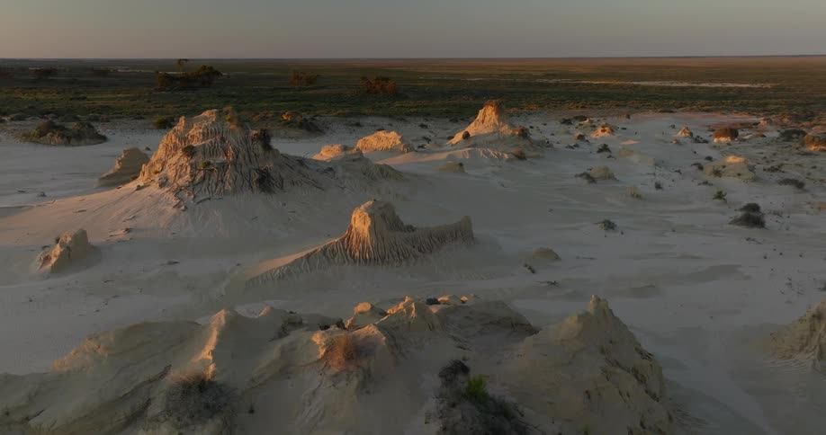 Ground covered with desert sand next to a grassland under a morning sky