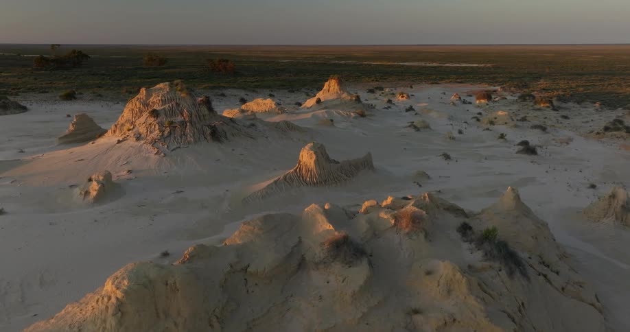 Aerial of white desert rock formations surrounded by white sand partially illuminated at sunset