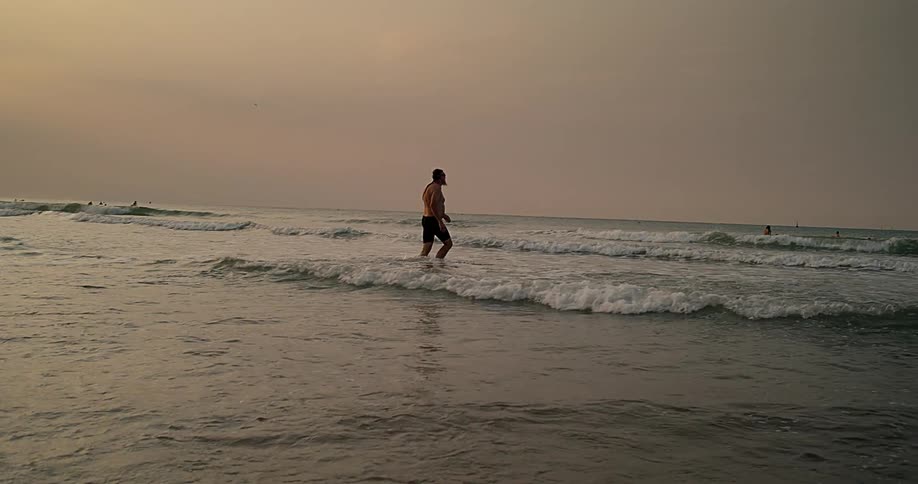 A man walks into the water at the beach as waves roll into shore