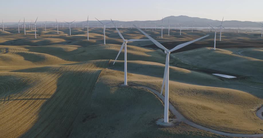 Wind turbines spin on a wind farm with mountains in the distance