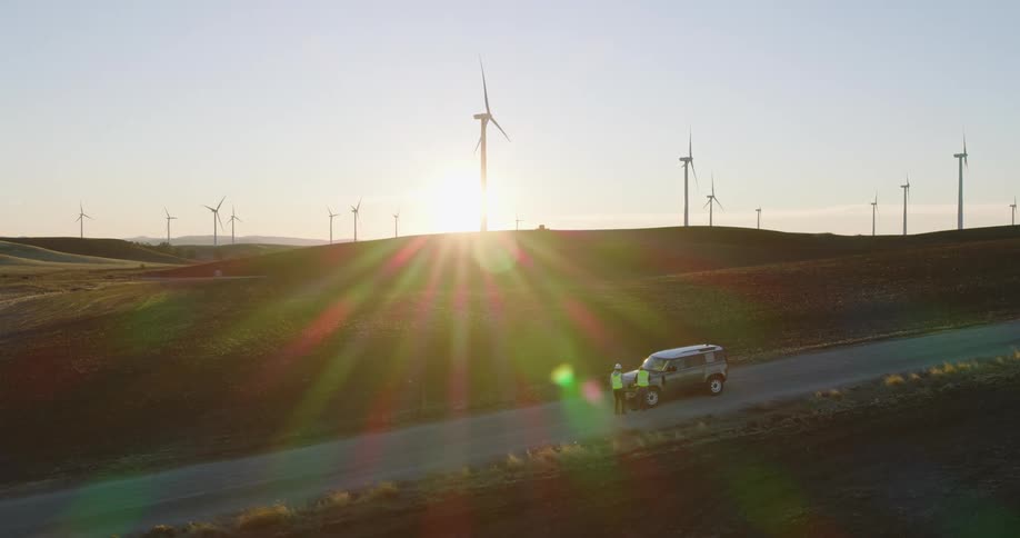 Two windfarm workers consult on highway near parked car