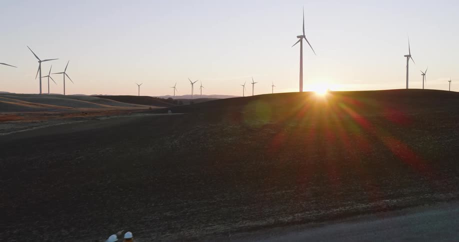 Workers are surveying the windmill farm at sunrise